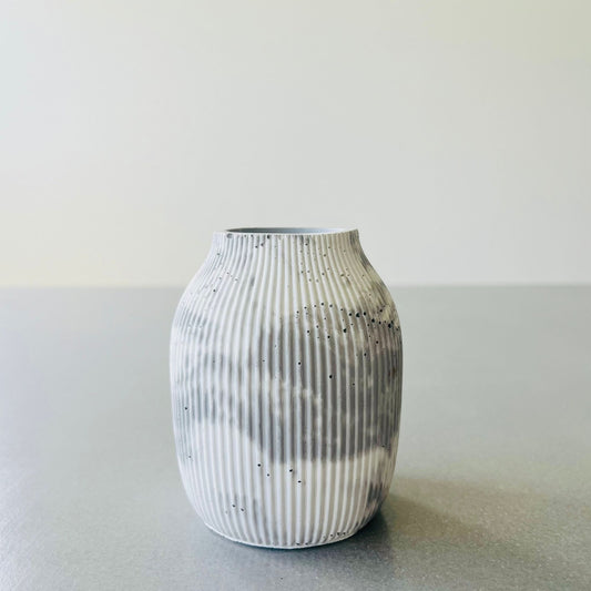 A small ribbed vase in Sea Drift, standing on a gray surface against a light gray background.