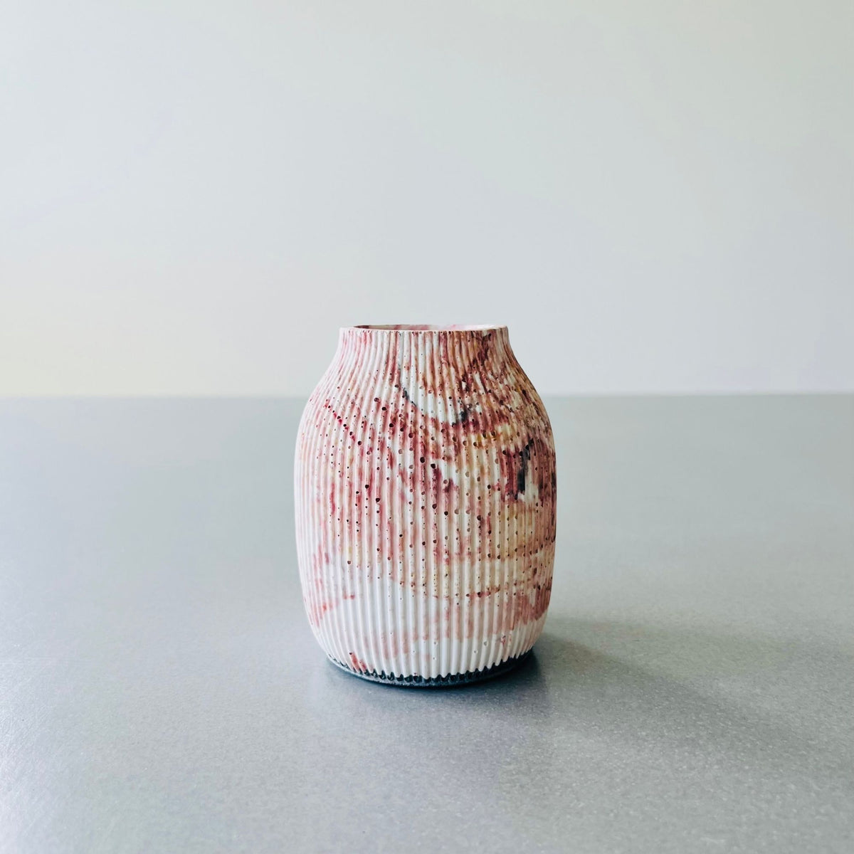 A small ribbed vase in Pilbara Marble Concrete finish, standing on a grey surface against a light grey background.